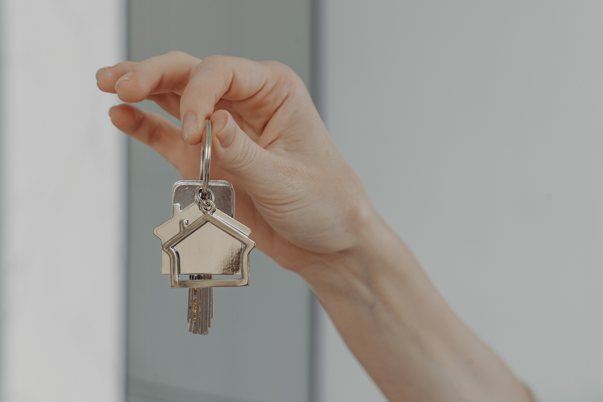 Woman holding house shaped keychain, selective focuse on female hand with key from new home